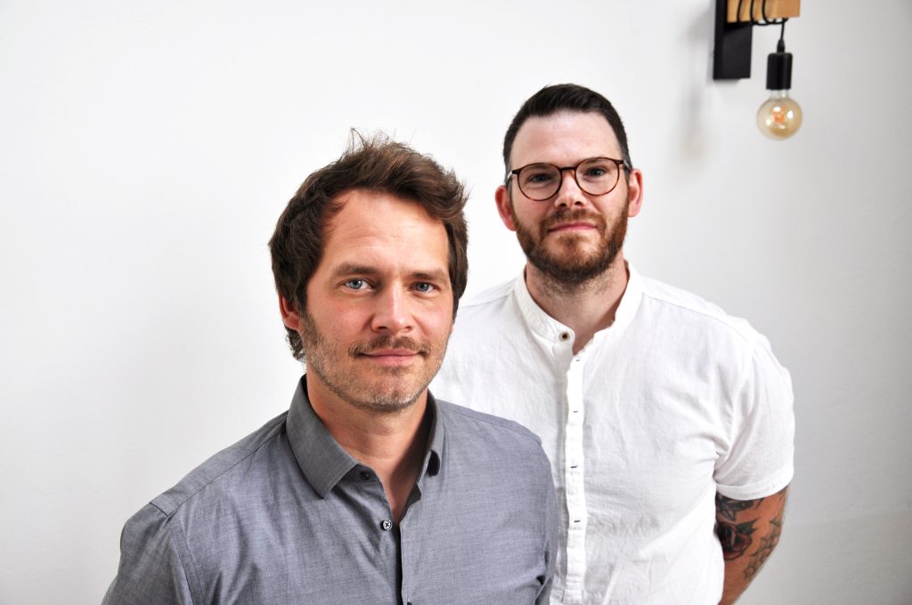 Hier sehen Sie ein Bild der beiden Gründer Daniel und Sebastian von akustik.inklusiv, beide schauen in die Kamera.